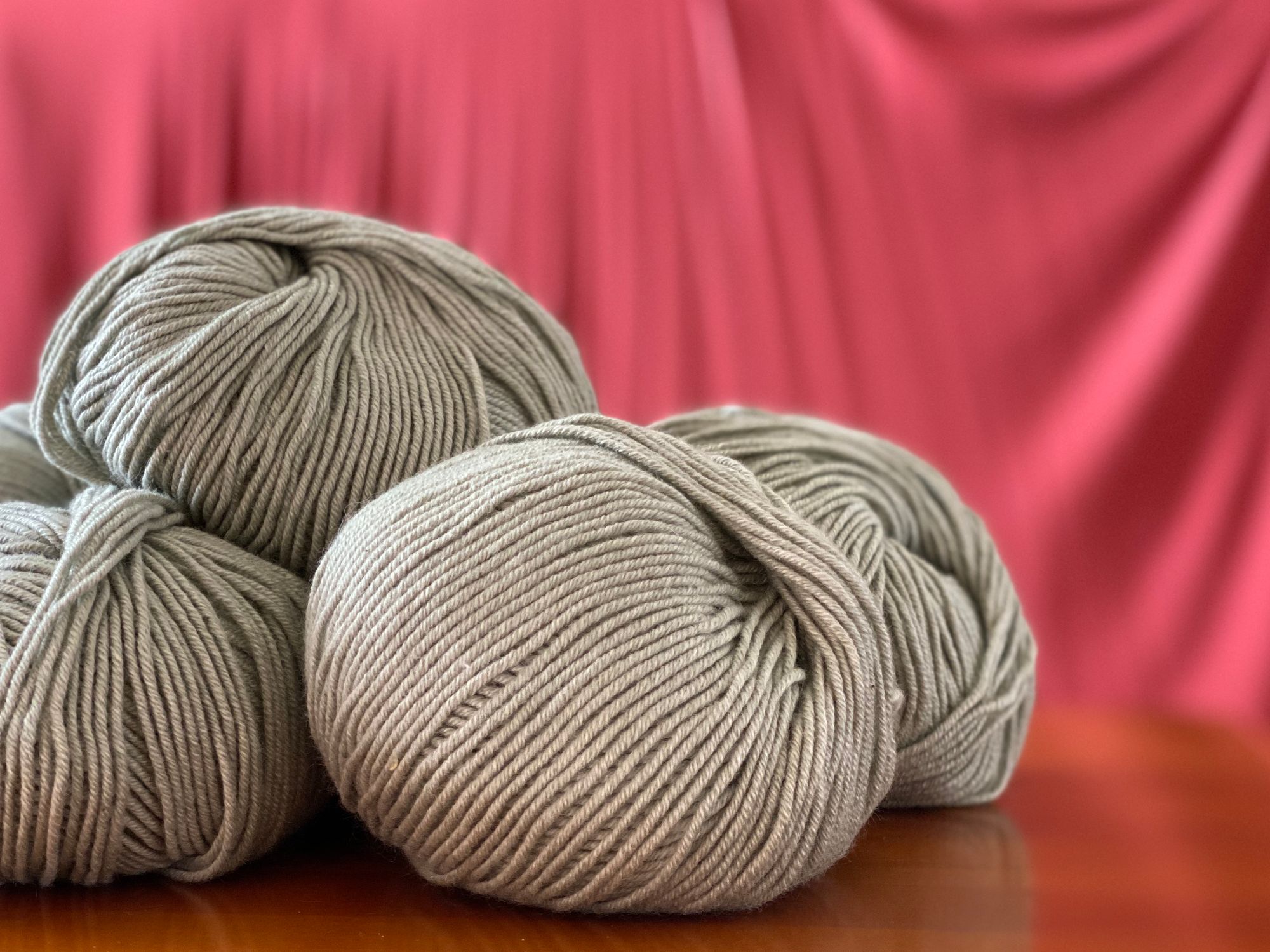 balls of yarn in a light sage green against a rich coral draped fabric background