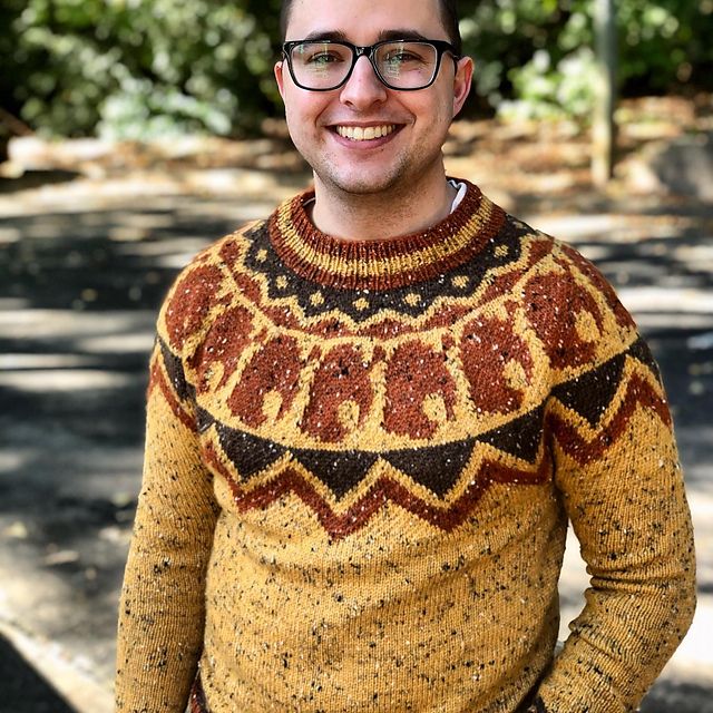 A man in a colorwork sweater made with tweed yarns in rich gold and browns smiles at the camera.