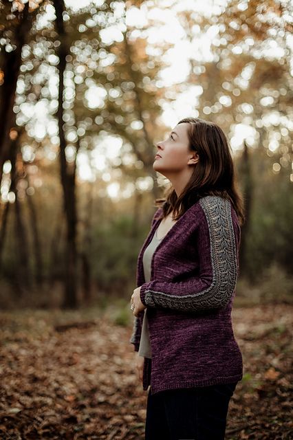 Profile of a woman in a moody forest, wearing a plum-colored cardigan with a grey lace panel down the sleeve.