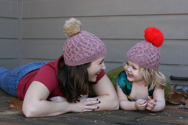 Christina and Marlowe smiling at each other in their matching Habitat hats with giant pom poms