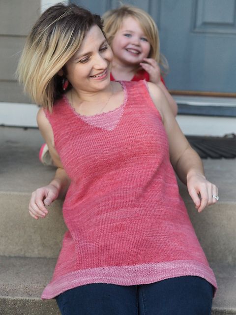 Christina and Marlowe, smiling on their porch, Christina wearing a pink handknit tunic