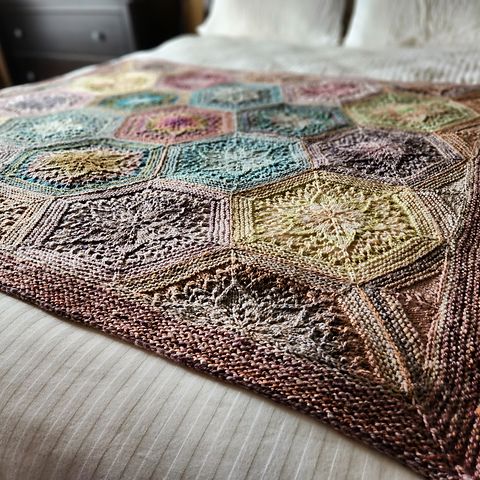 a hexagon motif blanket knit in many different kinds of handspun yarns, all in subtle tones of blue, pink, grey, yellow, and plum