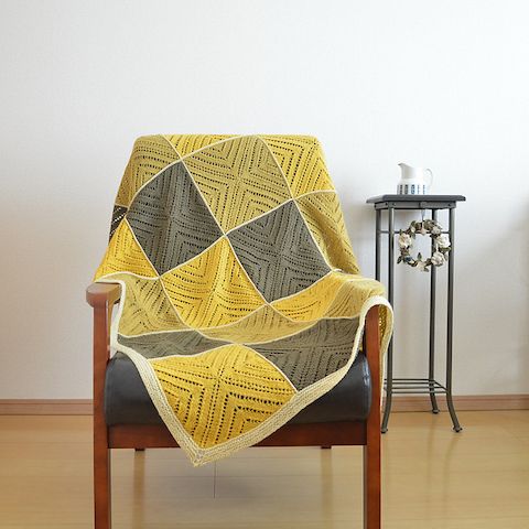 a sleek and sunny room with an iron table and wooden chair. on the chair lies a blanket in naturally-dyed shades of yellow, green, grey, and cream