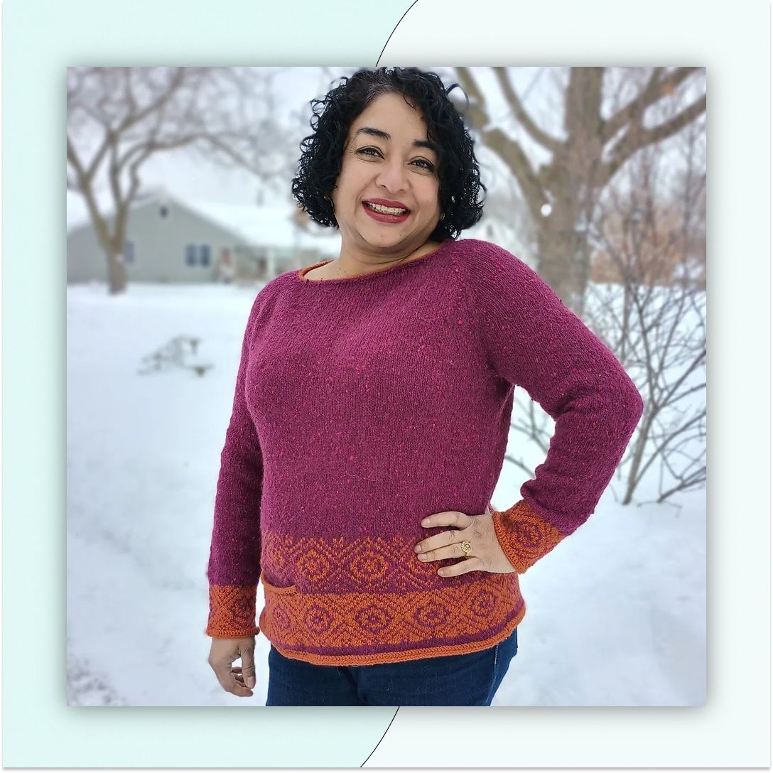 A smiling woman stands outside in the snow, wearing a fuschia sweater with colorwork in bold orange.