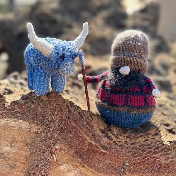 Miniature handknit Babe the Blue Ox with a Gnome Paul Bunyan, on top of a sideways stump.