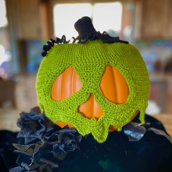 A pumpkin on a pedastal, with a crocheted covering made to look like a green jack-o-lantern skull.