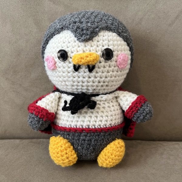 An adorable amigurumi penguin, crocheted to look as though it is wearing a Count Dracula costume