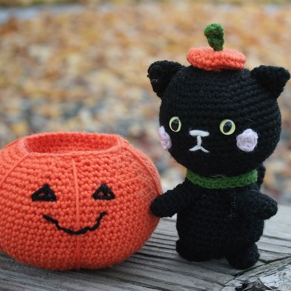 A smiling orange amigurumi pumpkin with a little black amigurumi cat wearing a pumpkin top hat.