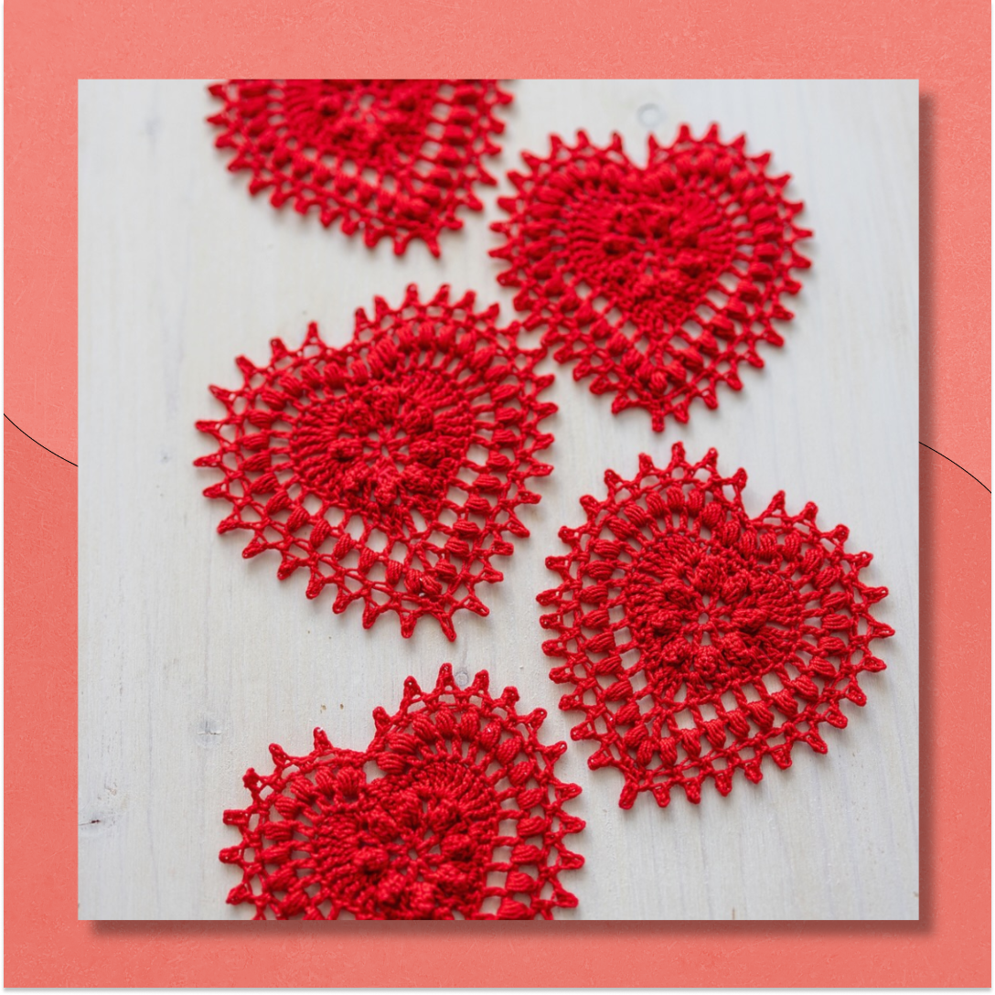 delicate, lacy crocheted red hearts with bobbles against a pale wood background