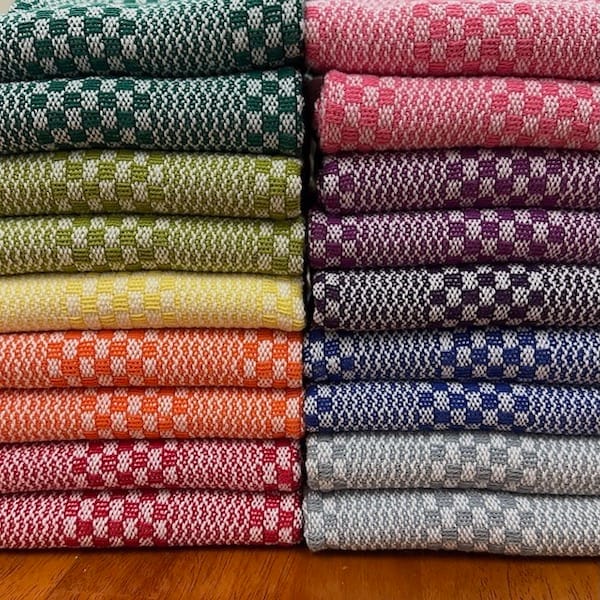two gorgeous stacks, side by side, of colorful tea towels in greens, yellow, orange, red, pink, purple, blue, and grey