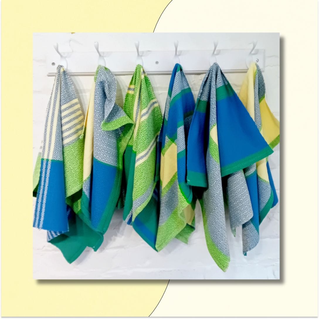Hanging woven towels in bright geometric patterns with cerulean and navy blue, grass and lime green, yellow, and cream.