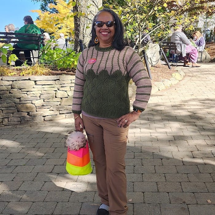 A woman stands on a path at the NY Sheep and Wool Festival, wearing a crocheted sweater with textured diamonds and contrasting stripes.