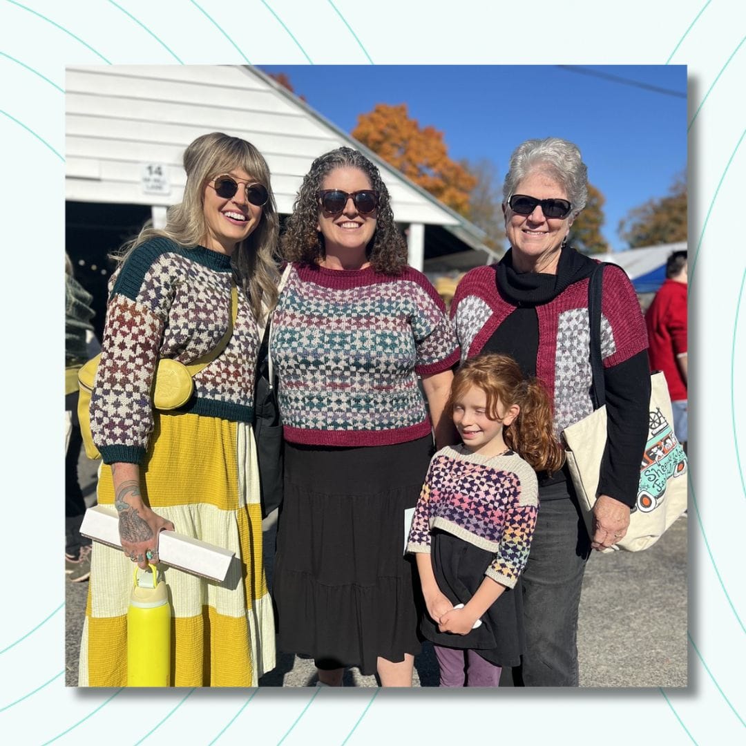 Three smiling women and a young girl stand beaming in the sunshine, all wearing stranded Framed sweaters.