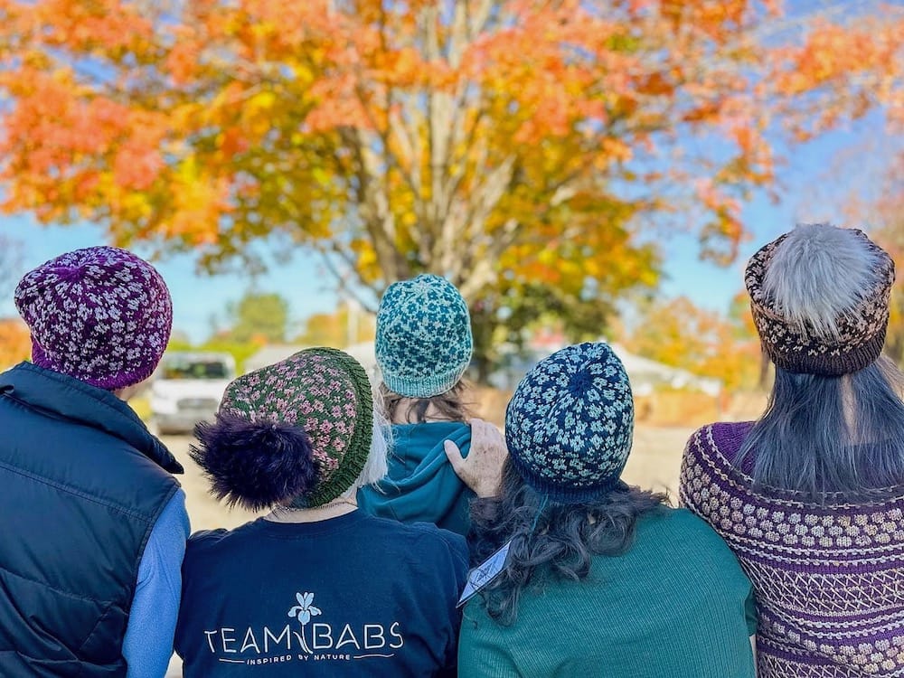 Five people stand looking away from the camera, wearing matching hats with stranded colorwork in a floral design.