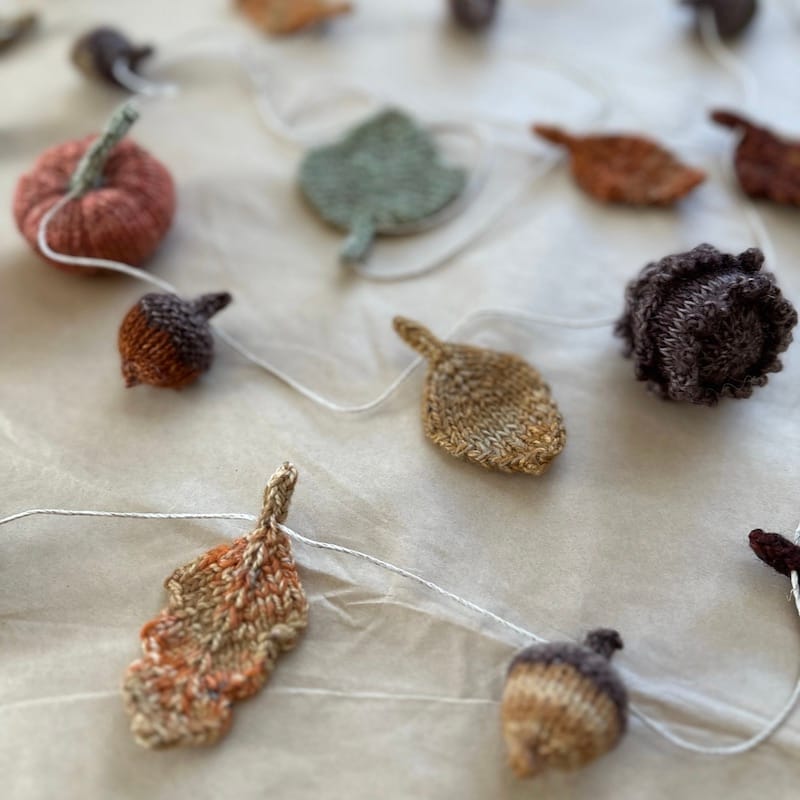 Charming handknit autumn motifs strung as a bunting: acorns, leaves, pumpkins, and pine cones.