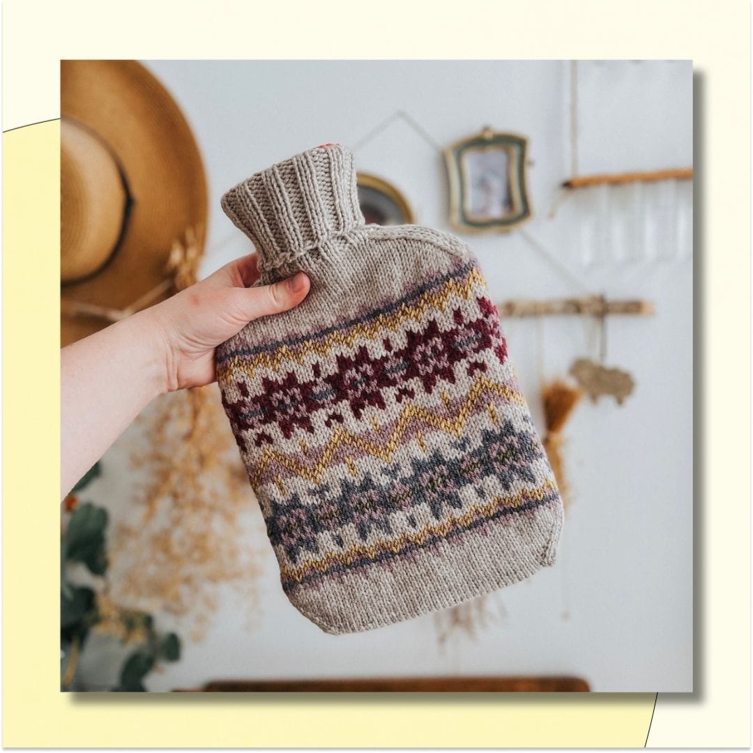 hand holding a stranded knit hot water bottle cover, with geometric designs in neutral colors