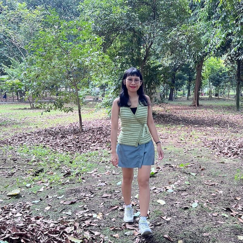 a person walks in a wooded field, smiling, wearing a green striped wrap tank