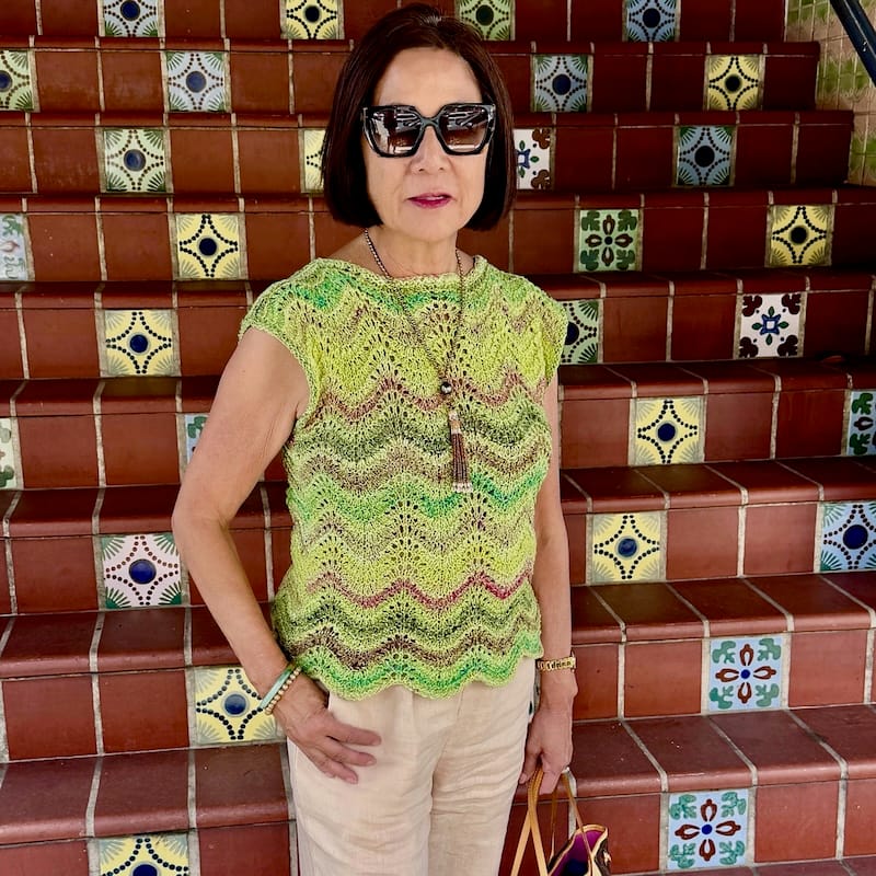 a person stands on a boldy patterned tile staircase, wearing a bright green striped feather-and-fan top